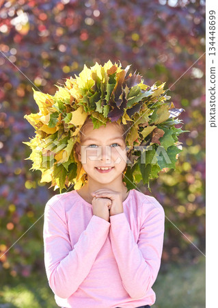 Smiling caucasian female child with leaf crown in autumn setting Smiling caucasian female child with leaf crown in autumn setting 134448699