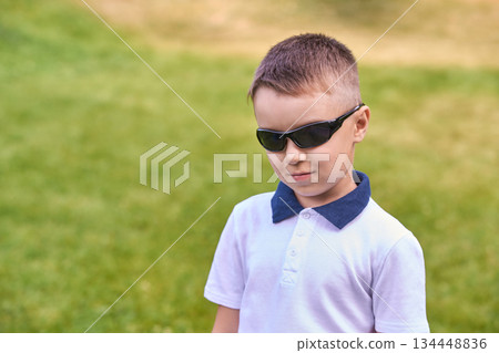 Confident caucasian young boy in sunglasses standing on grass looking cool Confident caucasian young boy in sunglasses standing on grass looking cool 134448836