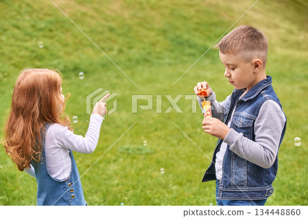 Caucasian children playing with bubbles on grass in casual clothing on a sunny Caucasian children playing with bubbles on grass in casual clothing on a sunny 134448860