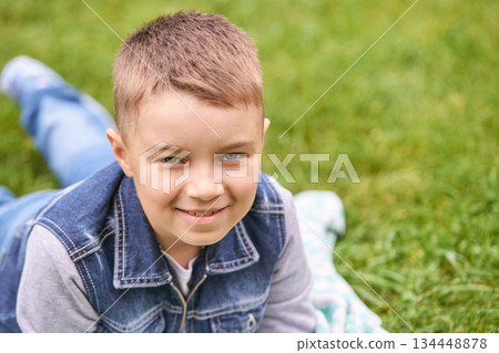 Smiling caucasian male child lying on grass in denim jacket relaxed outdoors Smiling caucasian male child lying on grass in denim jacket relaxed outdoors 134448878