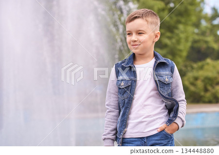 Smiling caucasian boy in denim jacket standing by fountain on sunny day Smiling caucasian boy in denim jacket standing by fountain on sunny day 134448880