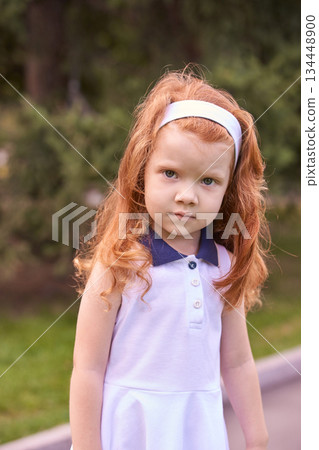Caucasian female child with red hair in white dress outdoors in a park setting 134448900
