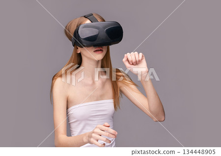 Young caucasian female experiencing virtual reality with vr headset on gray Young caucasian female experiencing virtual reality with vr headset on gray 134448905