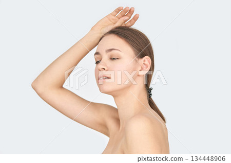 Young caucasian female with neutral expression poses gracefully against a plain 134448906
