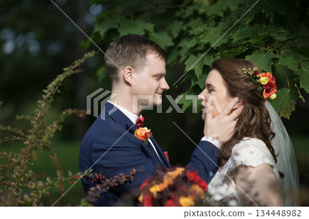 Groom gently touching brides face under green foliage 134448982