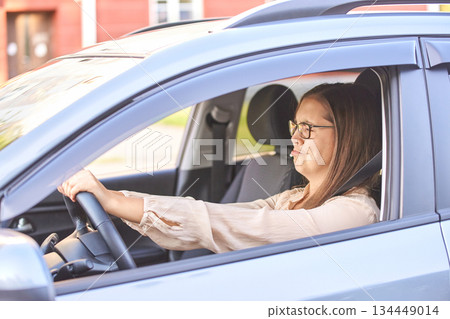 Young caucasian woman driving car with focused expression in suburban Young caucasian woman driving car with focused expression in suburban 134449014