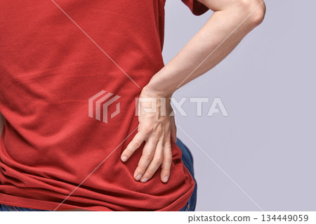 Person in red shirt experiencing back pain holding lower back with hand Person in red shirt experiencing back pain holding lower back with hand 134449059