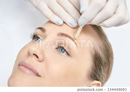 Caucasian female receiving eyebrow waxing treatment close-up with applicator Caucasian female receiving eyebrow waxing treatment close-up with applicator 134449091