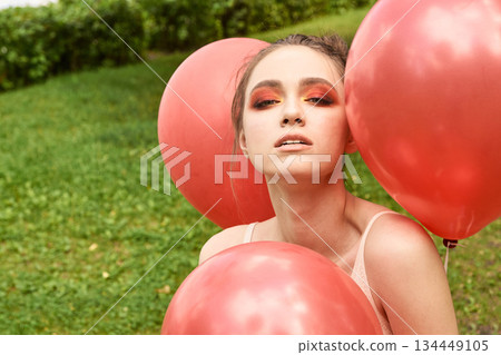 Young caucasian female with red balloons and bold makeup in outdoor garden Young caucasian female with red balloons and bold makeup in outdoor garden 134449105