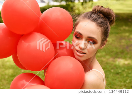 Young caucasian female with red balloons in outdoor park setting smiling 134449112