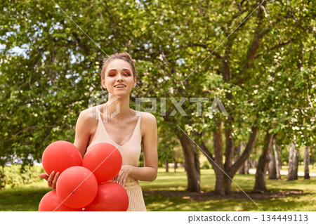 Young caucasian female with red balloons outdoors in a sunlit park Young caucasian female with red balloons outdoors in a sunlit park 134449113