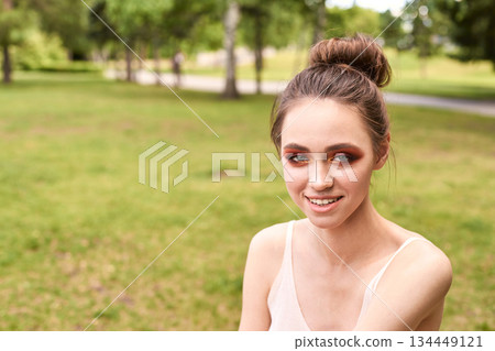 Smiling young caucasian female with bun in relaxing park setting on a sunny day 134449121
