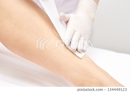 Female leg waxing procedure in beauty salon with protective glove and wax strip 134449123