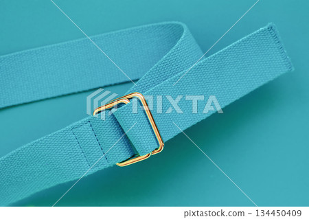 Minimal blue turquoise belt with golden metal buckle on matching cyan background, top view. Concept of modern accessories, fashion essentials, trendy color palette. Abstract bright modern background Minimal blue turquoise belt with golden metal buckle on matching cyan background, top view. Concept of modern accessories, fashion essentials, trendy color palette. Abstract bright modern background 134450409