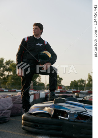A confident go-kart racer strikes a powerful pose beside his kart on the track 134450442