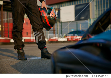 A racer holds their helmet in a vibrant pit lane setting 134450446