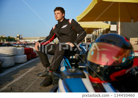 An aspiring racer poses confidently next to a gokart 134450460
