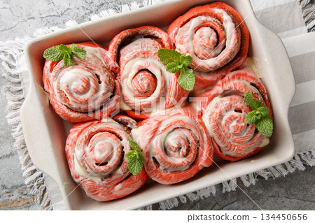 Festive pink cinnabons, cinnamon rolls with white icing, close-up in a baking pan. Horizontal top view Festive pink cinnabons, cinnamon rolls with white icing, close-up in a baking pan. Horizontal top view 134450656