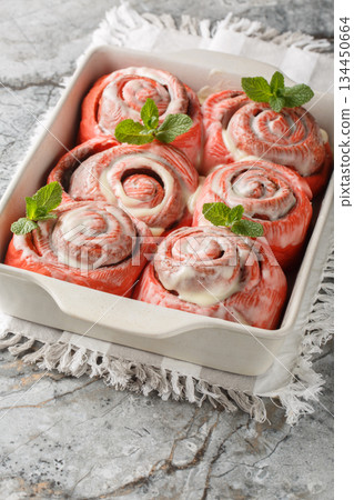 Close-up of pink cinnamon rolls with white icing in a baking dish. Vertical 134450664
