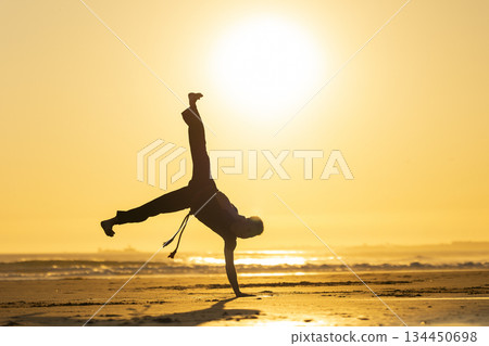 Man performing capoeira handstand on beach at sunset 134450698