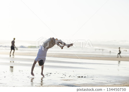 Young man performing backflip on beach during summer vacation 134450730