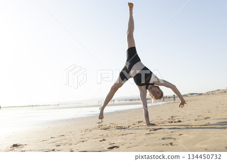 Woman performing cartwheel on beach sand Woman performing cartwheel on beach sand 134450732
