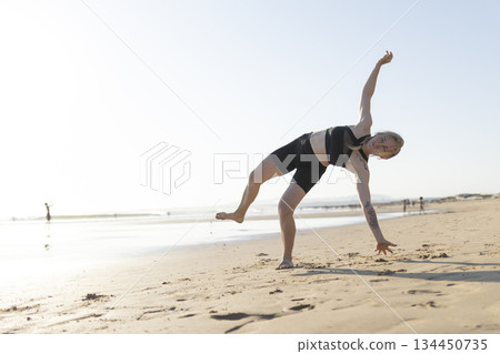 Woman balancing in half moon pose on sunny beach 134450735