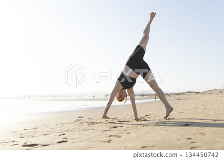 Woman practicing yoga pose on sandy beach 134450742