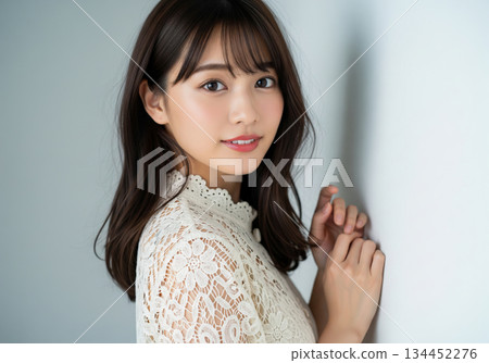 一位身穿蕾絲襯衫的美麗女子靠在牆上，面帶溫柔的微笑。 134452276