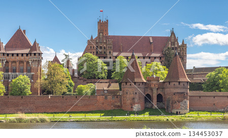 Malbork Castle, a brick Gothic castle in northern Poland, Europe. Magnificent medieval castle, a testament to history and architecture, stands proudly against a backdrop of blue sky and lush greenery. 134453037