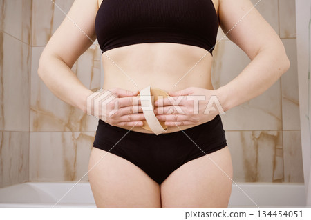 Woman performing dry body brushing on her abdomen for skin care and wellness 134454051
