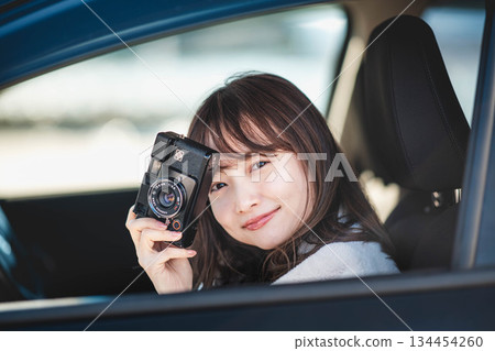 一位長髮年輕女子坐在汽車副駕駛座上，手裡拿著一台相機。 134454260