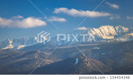 Tatra Mountains above Zakopane town in Poland, Europe. Panoramic views of a rugged mountain range with snow-dusted peaks under a bright blue sky, a tranquil and majestic landscape. 134454346