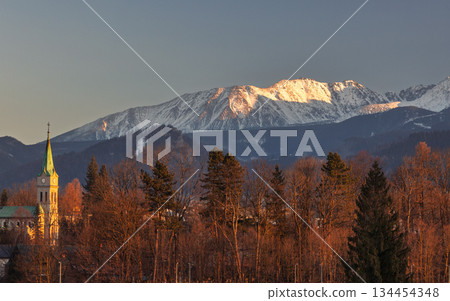 A serene landscape showcases a church steeple, a forest, and majestic, snow-capped mountains basking in the sunlight. Zakopane town at the foot of the Tatra Mountains in Poland, Europe. A serene landscape showcases a church steeple, a forest, and majestic, snow-capped mountains basking in the sunlight. Zakopane town at the foot of the Tatra Mountains in Poland, Europe. 134454348