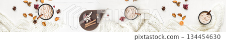 Panoramic top view of two mugs of hot chocolate with marshmallows, surrounded by cinnamon sticks, spices, and a warm white knitted scarf on a white wooden table. Panoramic top view of two mugs of hot chocolate with marshmallows, surrounded by cinnamon sticks, spices, and a warm white knitted scarf on a white wooden table. 134454630