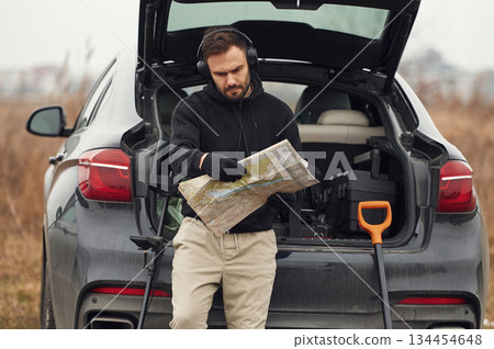 With map in hands, near automobile. Man is with metal detector in the field With map in hands, near automobile. Man is with metal detector in the field 134454648