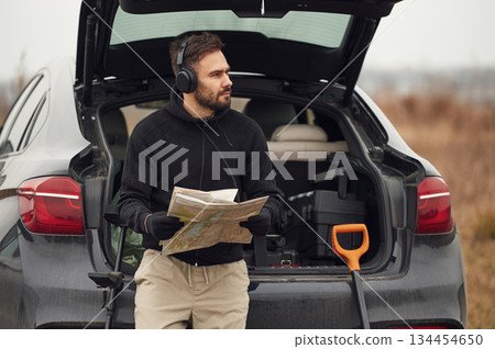 With map in hands, near automobile. Man is with metal detector in the field With map in hands, near automobile. Man is with metal detector in the field 134454650