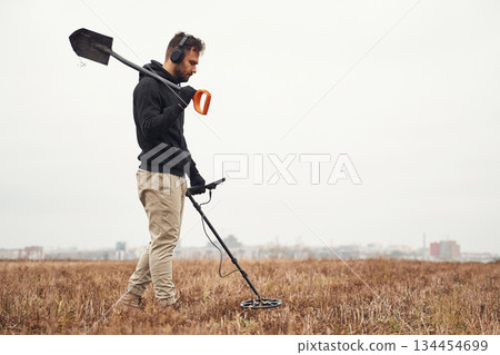 Holding a shovel. Man is with metal detector in the field Holding a shovel. Man is with metal detector in the field 134454699