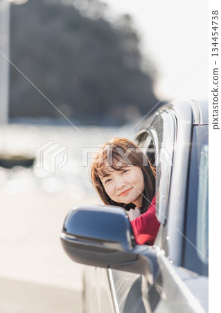 A young woman in a red knitted sweater leans forward in her car seat 134454738