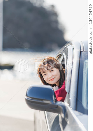A young woman in a red knitted sweater leans forward in her car seat 134454739