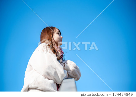 A young woman with long hair and a white coat against the blue sky 134454849