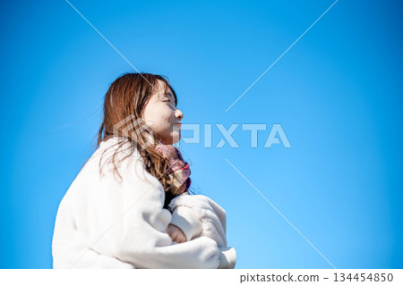 A young woman with long hair and a white coat against the blue sky 134454850
