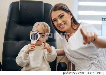 Sitting with doctor. Little boy is having check up in the ophthalmologist cabinet 134454943