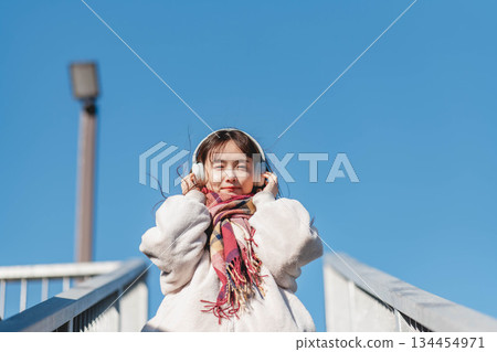 Smiling girl standing under the blue sky and listening to music 134454971