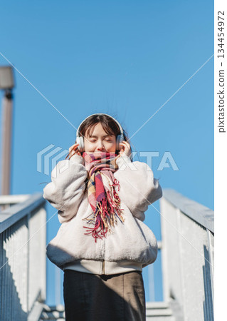 一位微笑的女孩站在藍天下,聽著音樂。 一位微笑的女孩站在藍天下,聽著音樂。 134454972