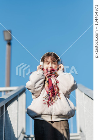一位微笑的女孩站在藍天下,聽著音樂。 一位微笑的女孩站在藍天下,聽著音樂。 134454973