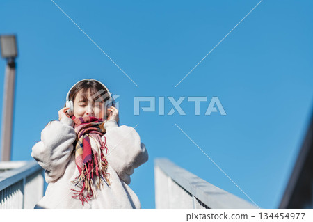 一位微笑的女孩站在藍天下，聽著音樂。 134454977