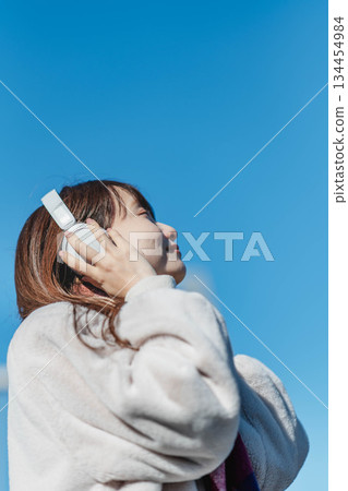Smiling girl standing under the blue sky and listening to music 134454984