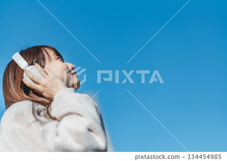 一位微笑的女孩站在藍天下,聽著音樂。 一位微笑的女孩站在藍天下,聽著音樂。 134454985