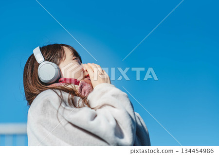 Smiling girl standing under the blue sky and listening to music 134454986